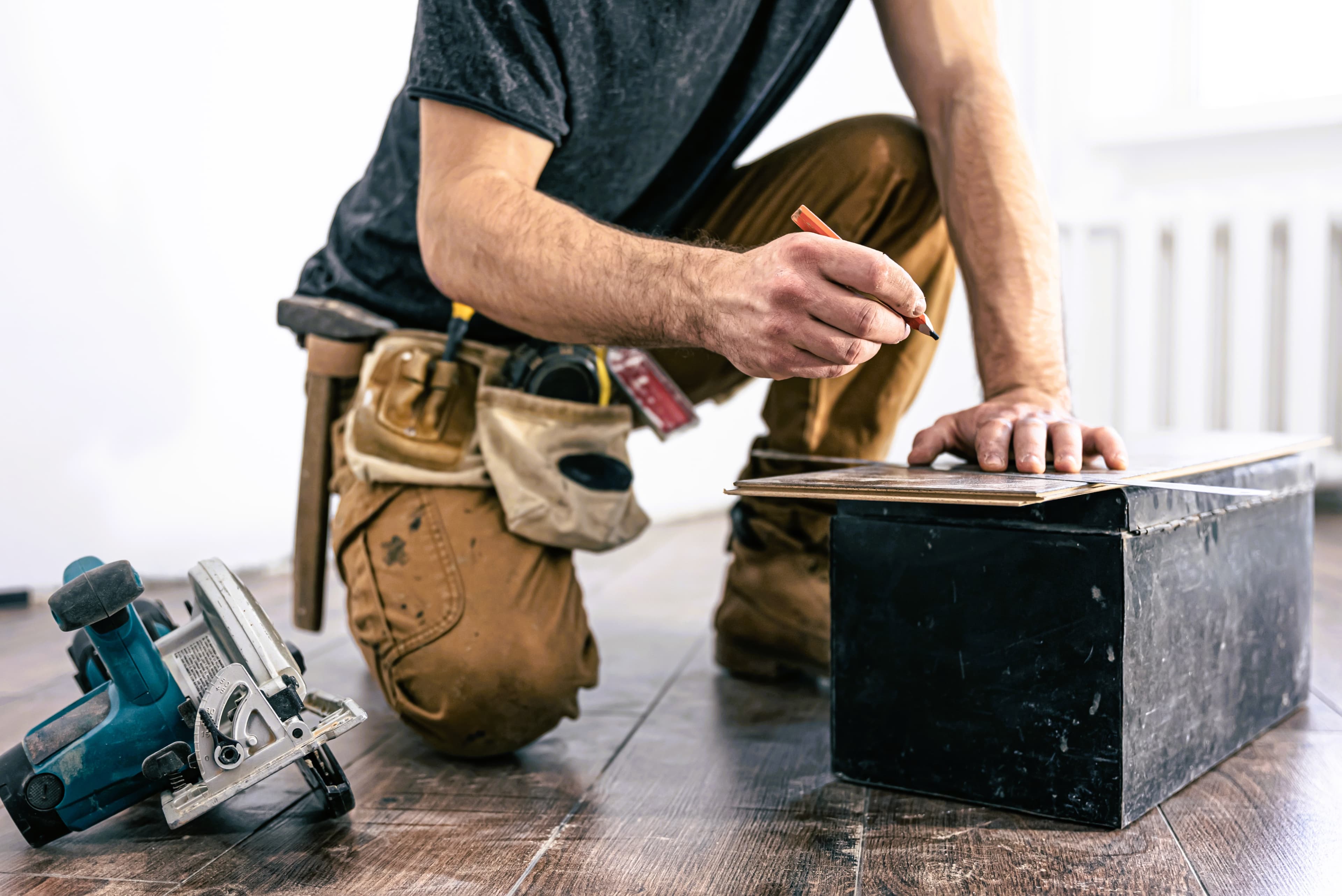 Carpenter marking wood flooring with circular saw and tool belt